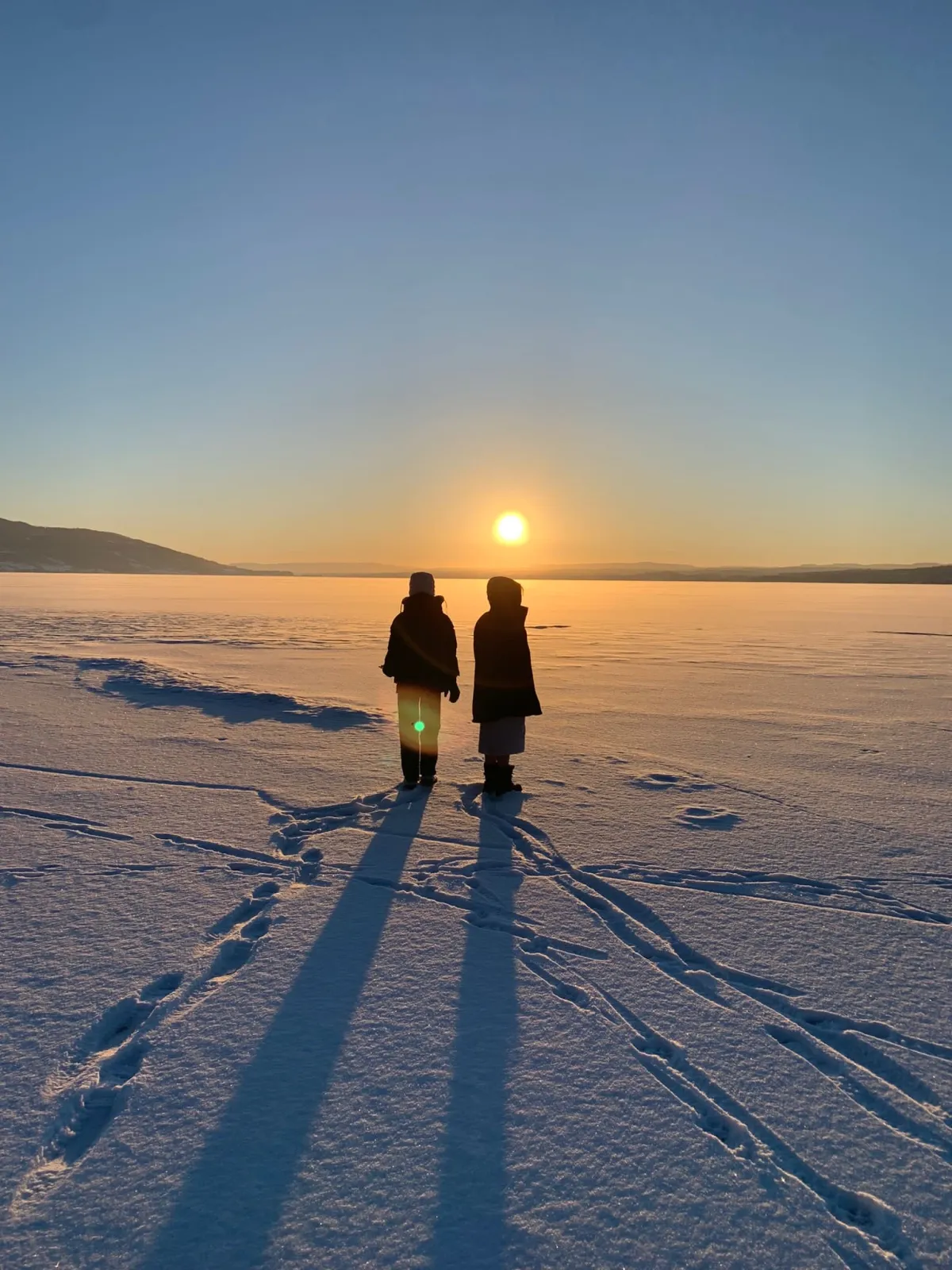 Zwei Jugendliche stehen bei Sonnenuntergang auf gefrorenem See