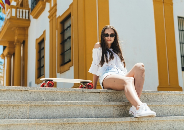 Junge Frau sitzt auf Steintreppe in sommerlichem, weissen Kleid mit Sonnenbrille