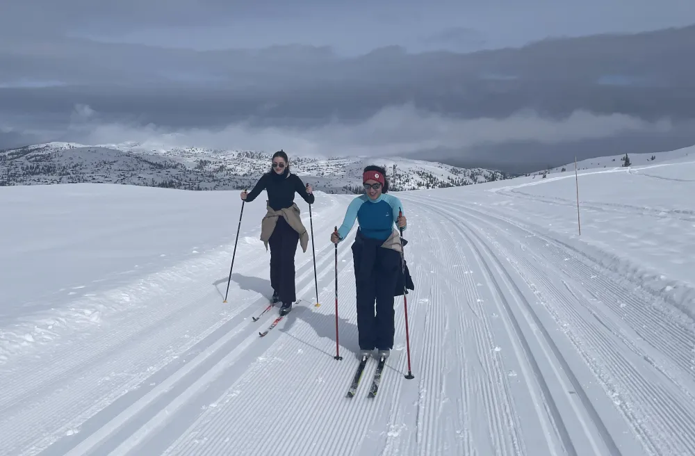 Zwei junge Frauen auf Langlaufski auf Piste mit blaugrauem Himmel